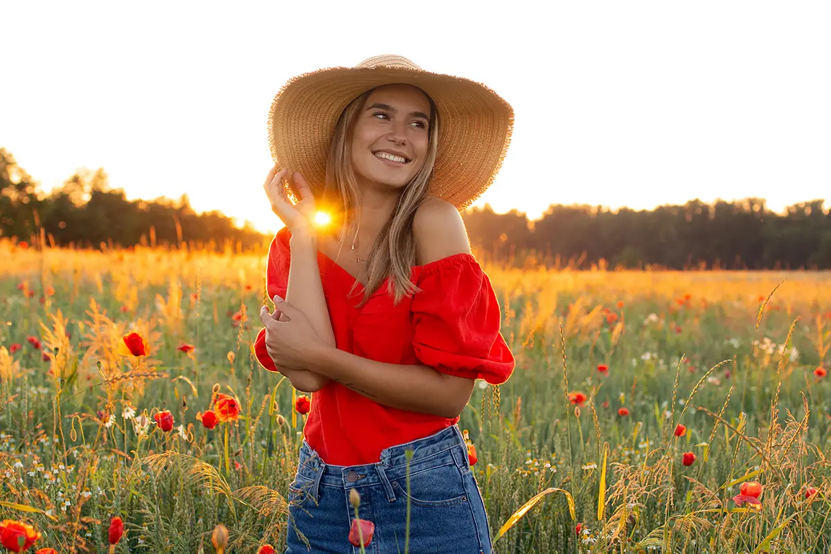Aileen steht lachend in einem Mohnfeld bei ihrem Portraitshooting während des Sonnenuntergangs.