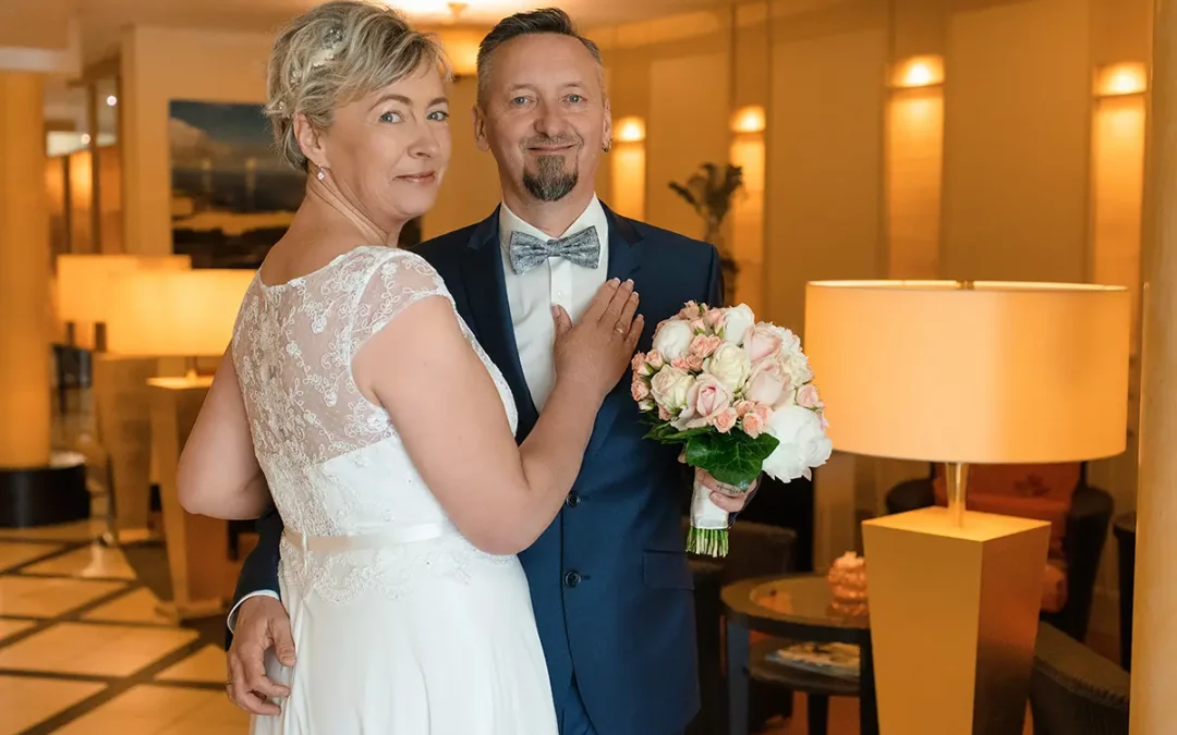 Ein Hochzeitspaar mit Brautstrauß steht stolz vor der Kamera.