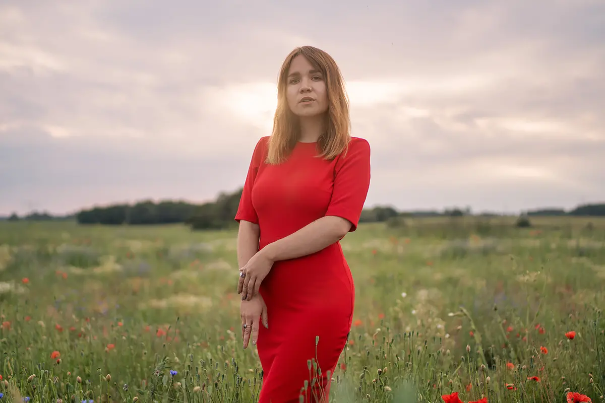 Cora steht bei ihrem Portraitshooting auf einem Feld in einem roten Kleid. Das Bild ist bearbeitet.